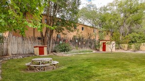 A grassy outdoor area with a wooden picnic table and a red door, surrounded by trees and a fence.