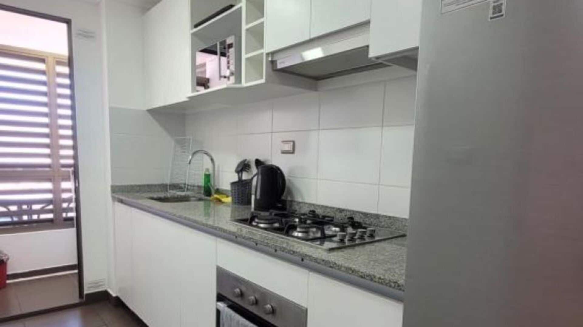 Una cocina con armarios blancos, una estufa a gas y una ventana con persianas.
