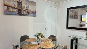 A dining area with a round table, chairs, a vase with flowers, and a painting on the wall.