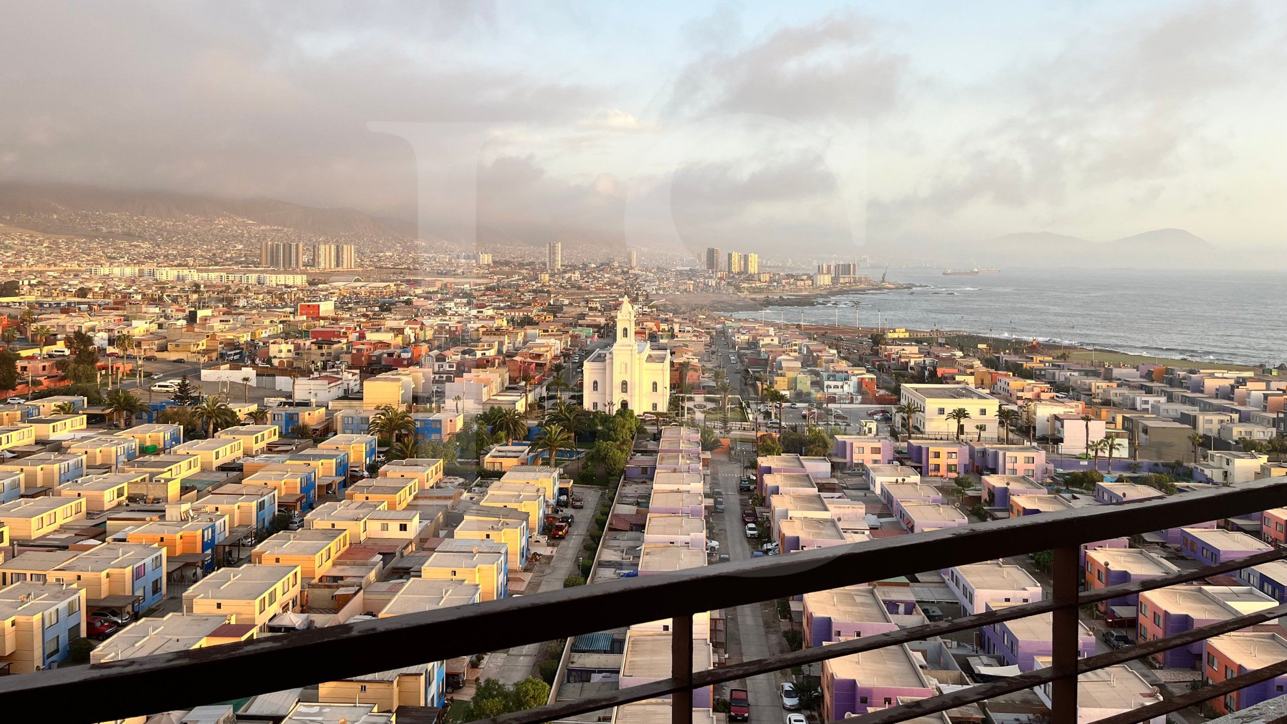 Paisagem costeira urbana com uma igreja imponente, edifícios residenciais densos e vista para o mar.