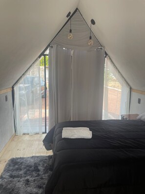 A bedroom with a black bed, white curtains, and a view of the outside.