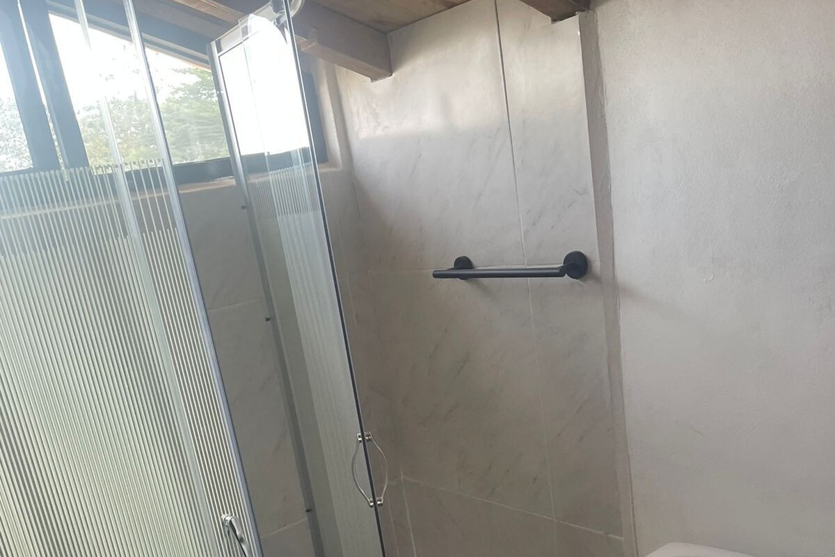 Et badeværelse med glasvæg omkring brusenichen, et hvidt toilet og en håndklædestang.