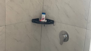 A shower area with a black shelf holding a box and a bottle, and a silver showerhead. - CABAÑAS ALDEA GOTICA (Amealco de Bonfil)