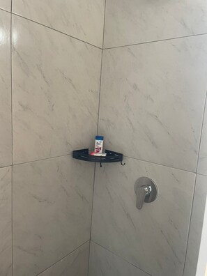 Et bruseområde med en sort hylde med en æske og en flaske, samt et sølvfarvet brusehoved.