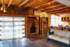 Un interior rústico con chimenea de ladrillo, vigas de madera, un sofá y una zona de cocina.