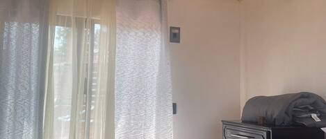 Une chambre avec un plafond en bois, un lit avec une literie noire, une table de chevet et une fenêtre ornée de rideaux légers.