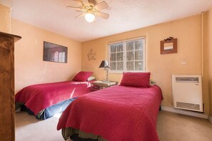 Une chambre avec deux lits, un ventilateur de plafond, une fenêtre et un radiateur.