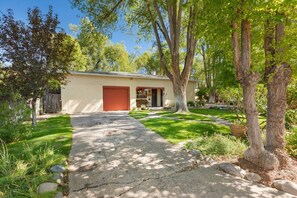 A single-story building with a red garage door, a front yard with a paved walkway, and mature trees.