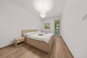 A bedroom with a wooden bed, a nightstand, a bedside table, a window with blinds, and a ceiling light. - AC 2 room apartment, Old City, Blumentalska (Bratislava)