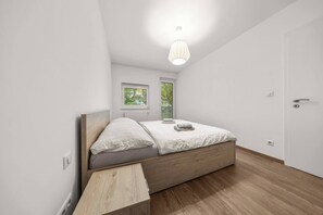 Ein Schlafzimmer mit einem Einzelbett, einem Nachttisch, einem Fenster mit Jalousien und einer Tür.