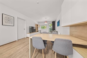 A modern dining area with a wooden table, grey chairs, a flat-screen TV, and a pendant light. - AC 2 room apartment, Old City, Blumentalska (Bratislava)