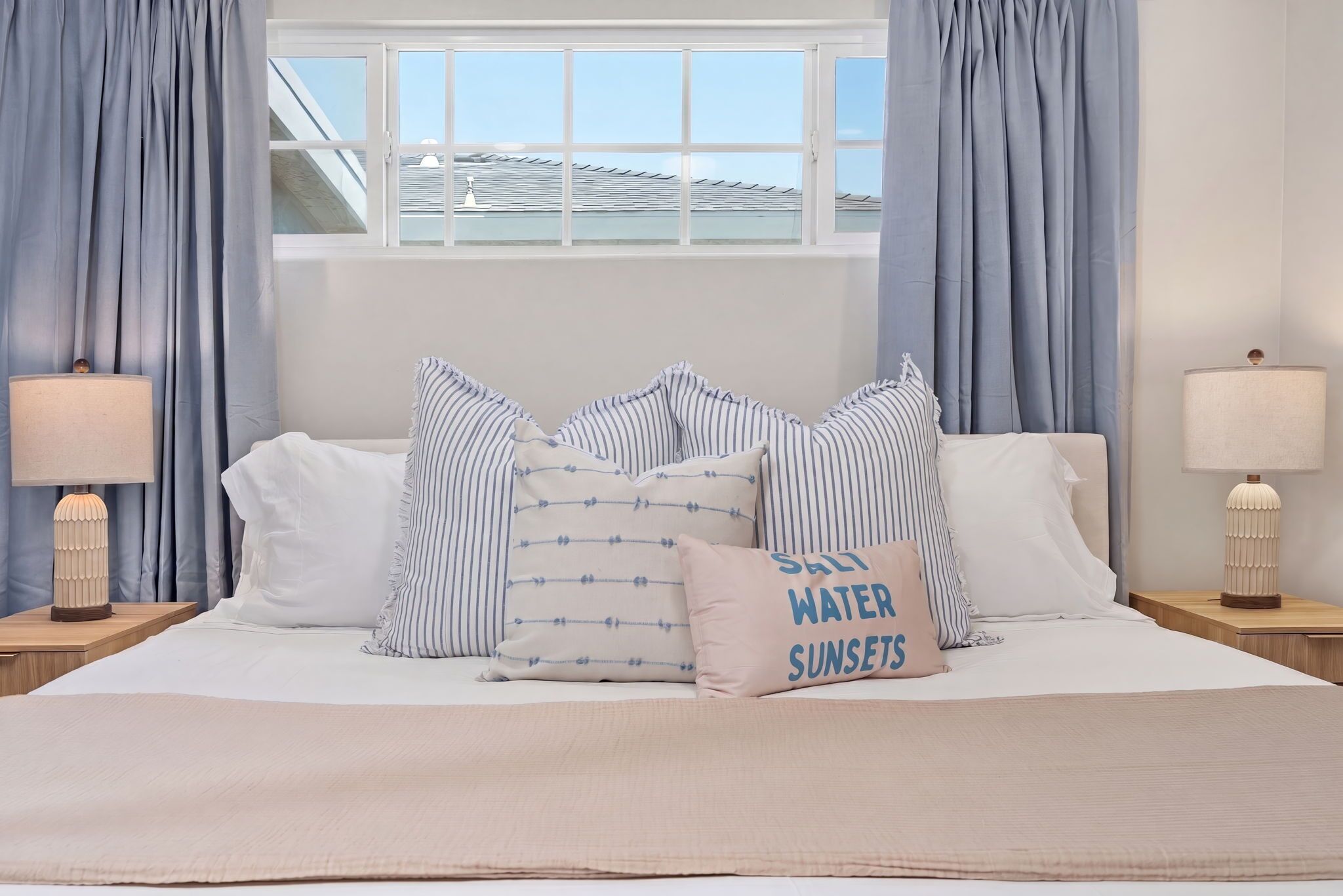 Una camera da letto con un letto, cuscini, una lampada da comodino e una finestra con tende.