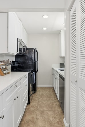 A compact kitchen with white cabinetry, a black refrigerator, a microwave, and a dishwasher. - Newport Beach & Bay Oasis 2 King Beds, Smart TVs, AC Bike Rentals & Beach Gear (Newport Beach)