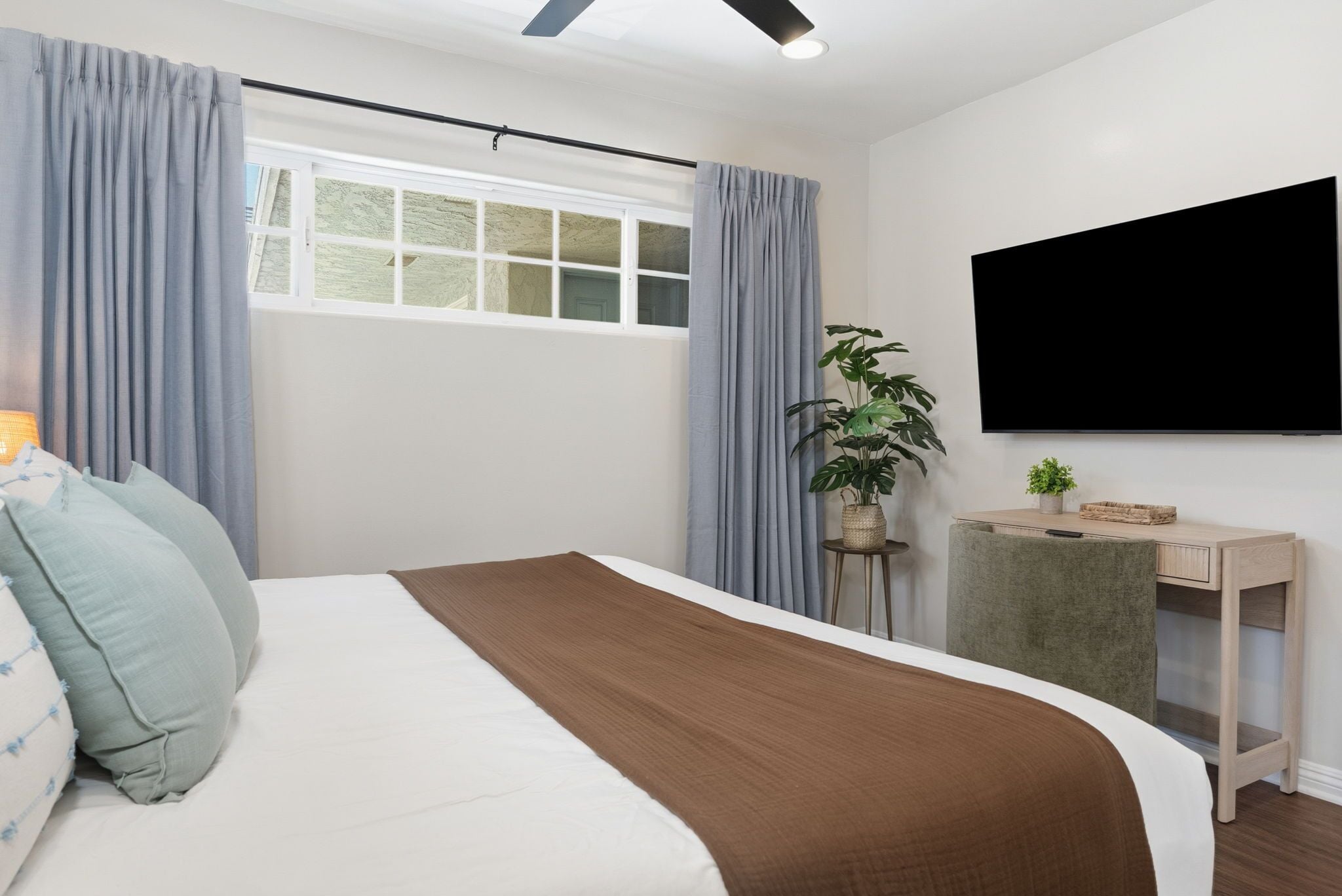 Una camera da letto moderna con un letto, tende, una scrivania, una pianta e una TV.