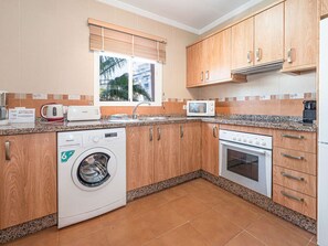 A compact kitchen with wooden cabinets, a built-in washing machine, a microwave, and a stove. - Apartment  by Interhome (Nerja)