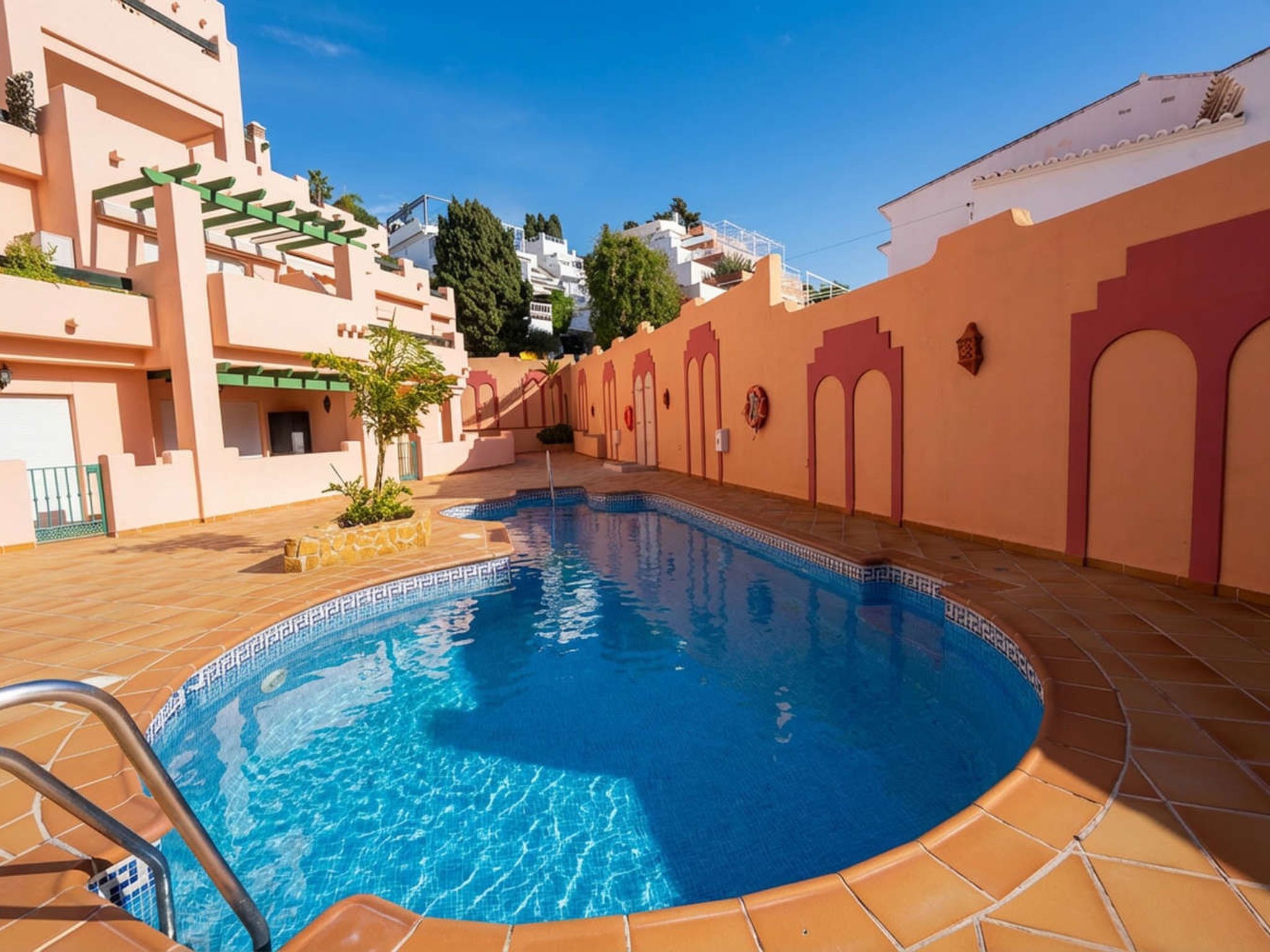 A swimming pool with a tiled deck, surrounded by buildings with Mediterranean architecture.