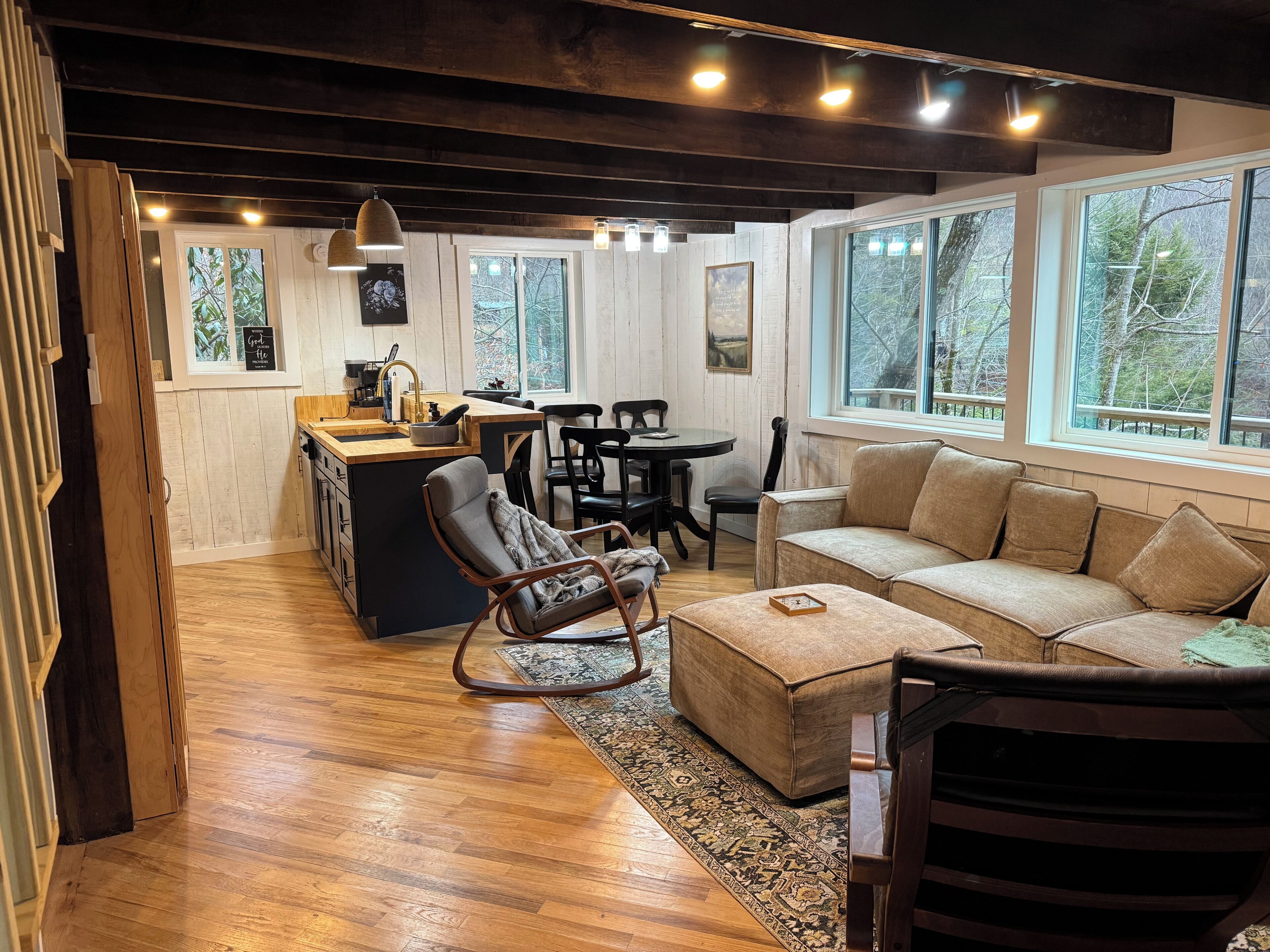 Un intérieur chaleureux avec un plancher en bois, un canapé, un fauteuil à bascule, une table à manger et un coin cuisine avec une fenêtre.
