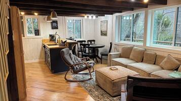 Un intérieur chaleureux avec un plancher en bois, un canapé, un fauteuil à bascule, une table à manger et un coin cuisine avec une fenêtre.