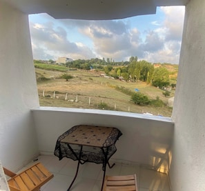 Un balcón con mesa y sillas, vista a un paisaje rural con árboles y edificios.