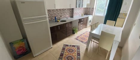 Cocina compacta con refrigerador, lavamanos y un pequeño comedor con sillas.