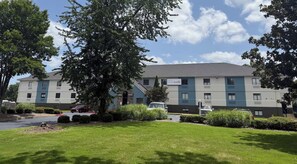 Ein mehrstöckiges Hotel mit flachem Dach, Parkplatz und gepflegtem Rasen.