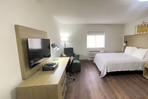 Ein Hotelzimmer mit Bett, Schreibtisch mit Computer, Fernseher, Stuhl, Lampe und Fenster.