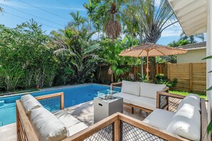 A poolside area with a wooden deck, white cushioned seating, and a glass-top table. - Fox Eden Resort 8Bd Pool Spa Oasis (Fort Lauderdale)