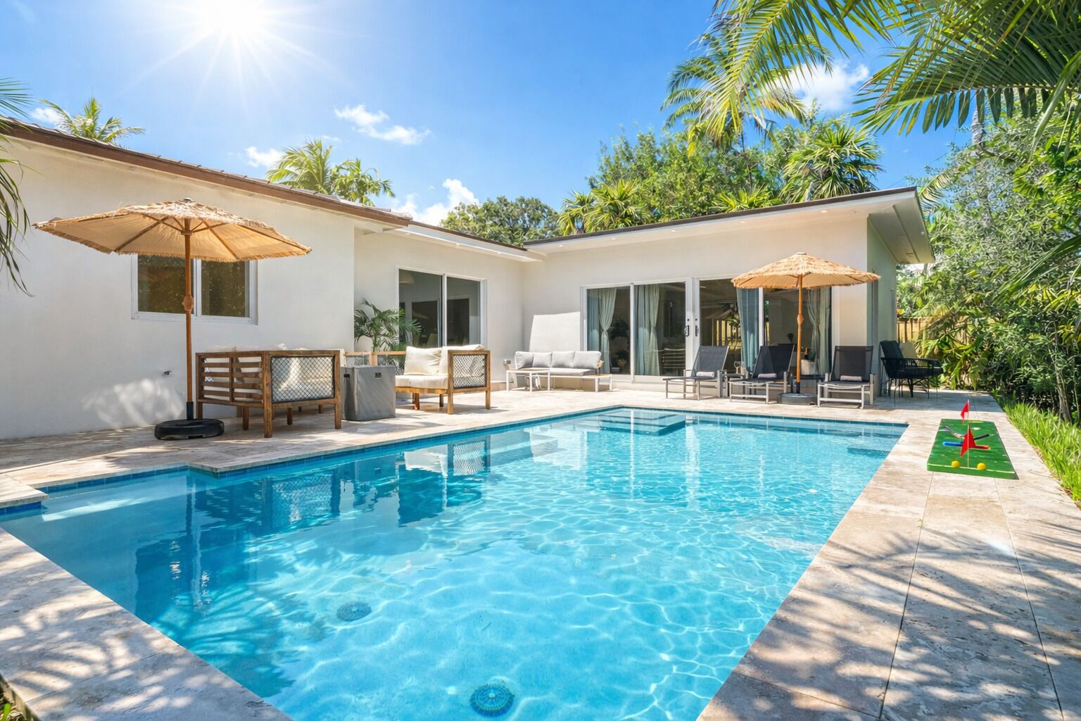 A swimming pool with lounge chairs and umbrellas, surrounded by a house and greenery.