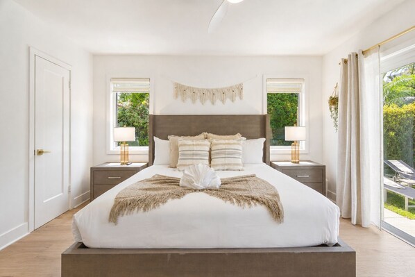 A bedroom with a large bed, two bedside tables with lamps, a headboard, and a view of greenery outside. - Fox Eden Resort 8Bd Pool Spa Oasis (Fort Lauderdale)