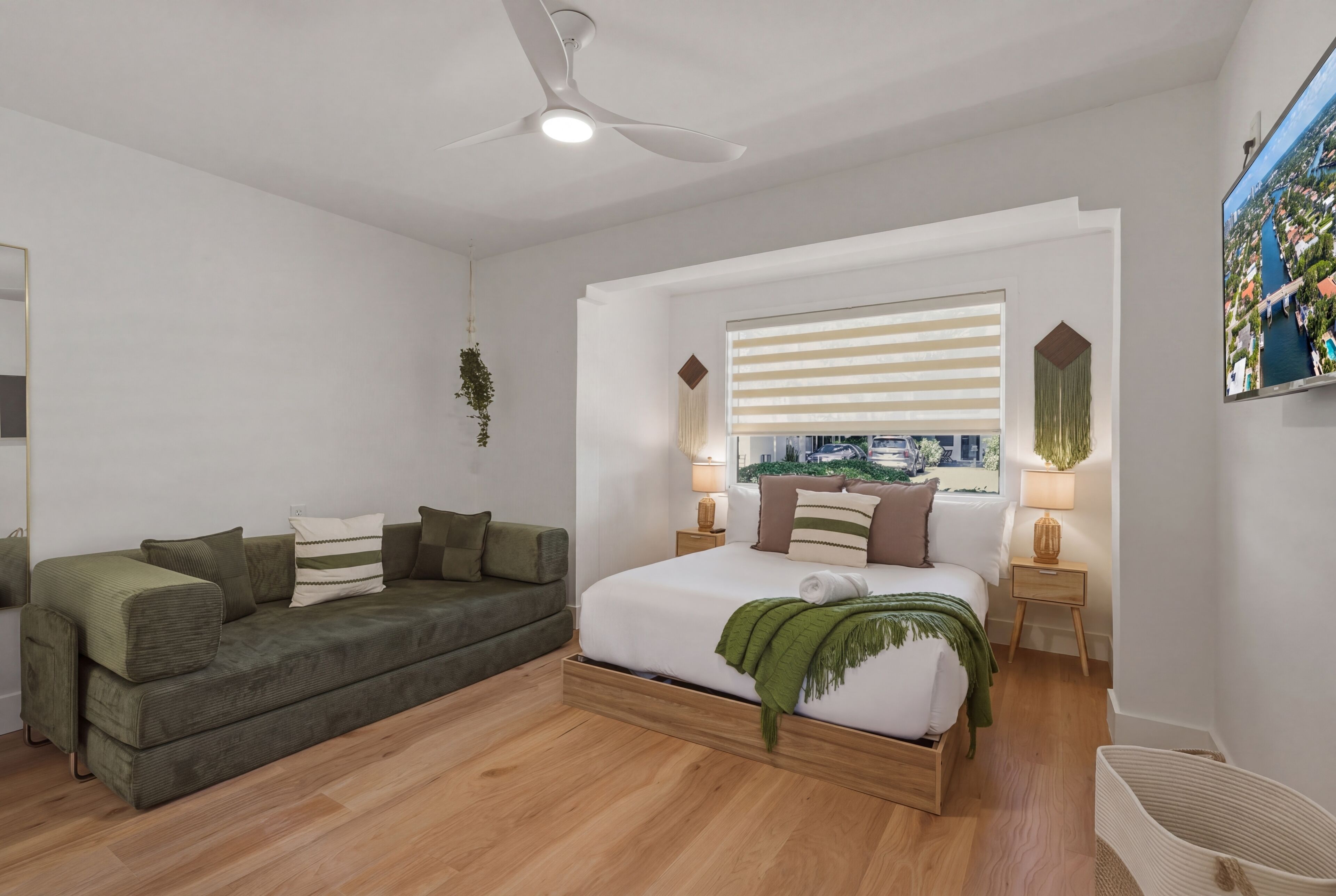 Une chambre à coucher moderne avec un lit, un canapé vert, un ventilateur de plafond et une fenêtre avec des stores.