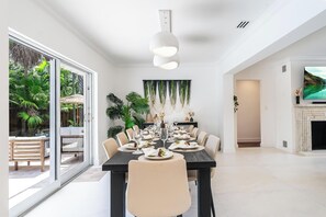 A modern dining room with a large table set for six, surrounded by chairs, with a view of a tropical garden through large windows. - Fox Eden Resort 8Bd Pool Spa Oasis (Fort Lauderdale)
