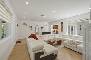A modern living room with a sectional sofa, a coffee table, and a dining area in the background. - Fox Eden Resort 8Bd Pool Spa Oasis (Fort Lauderdale)