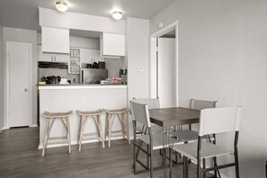A modern kitchen with white cabinetry, a central island, and a dining area with a wooden table and four bar stools. - Riverside escape | Pool & Gym | Free parking (Austin)