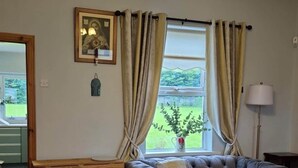 A living room with a sofa, a wooden side table, a lamp, and a window with curtains.