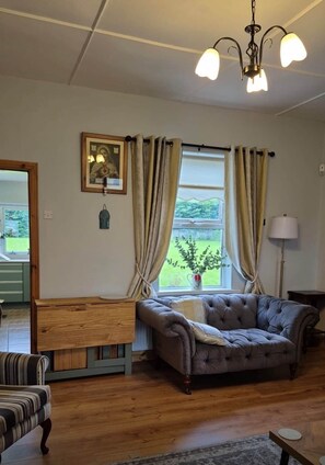 A living room with a sofa, a wooden side table, a lamp, and a window with curtains.