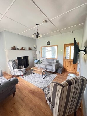 A living room with a fireplace, sofa, armchair, and a television mounted on the wall.