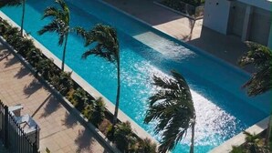 Ein modernes Hotel mit Pool, Palmen und blauem Himmel.