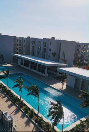 A modern hotel with a swimming pool, palm trees, and a clear sky. - Cartagena  Serena del Mar 2 habitaciones, cerca de la playa (Cartagena de Indias)