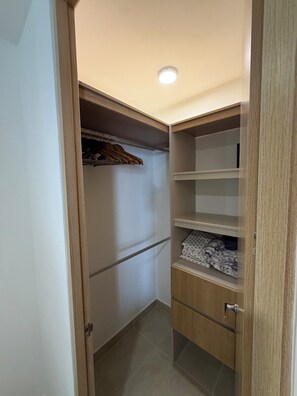 A small, enclosed closet with wooden doors and shelves, containing hanging clothes and folded items.