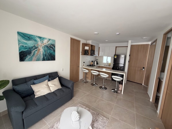 A modern living room with a sofa, a coffee table, and a kitchen area with a bar and stools.