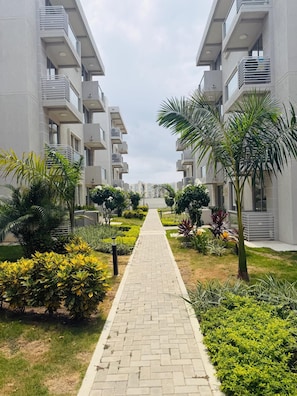 A pathway flanked by modern buildings with balconies, leading to a distant structure.