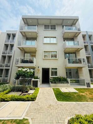 Un edificio residencial de varios pisos con entrada central, balcones y un jardín ajardinado.
