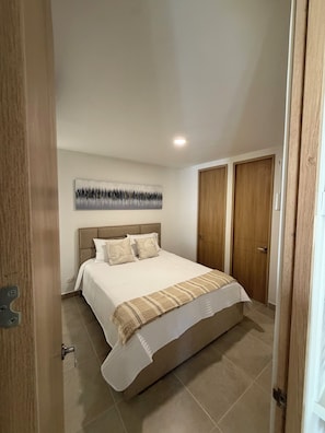 A bedroom with a bed, a headboard, a wall-mounted artwork, and a door. - Cartagena  Serena del Mar 2 habitaciones, cerca de la playa (Cartagena de Indias)