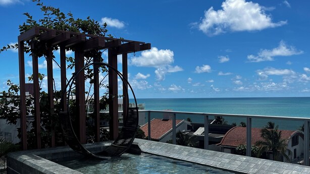 A clear blue sky, a swimming pool with a wooden pergola, and a view of the ocean. - Studio Beira Mar do Bessa (João Pessoa)