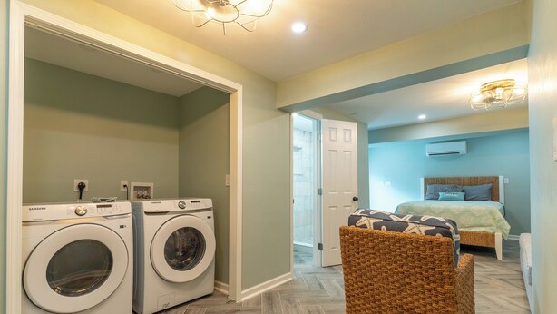 A compact room with a bed, a chair, and two washing machines. - Sunrise Serenity – Your Sanibel Island Retreat (Sanibel)