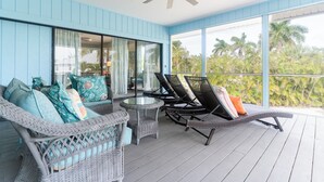 A covered outdoor seating area with wicker furniture, a glass table, and a ceiling fan. - Sunrise Serenity – Your Sanibel Island Retreat (Sanibel)