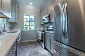 A modern kitchen with stainless steel appliances, a window with decorative items, and a wooden floor. - Sunrise Serenity – Your Sanibel Island Retreat (Sanibel)