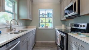 A kitchen with a built-in microwave, stainless steel appliances, and a window with a view of greenery. - Sunrise Serenity – Your Sanibel Island Retreat (Sanibel)