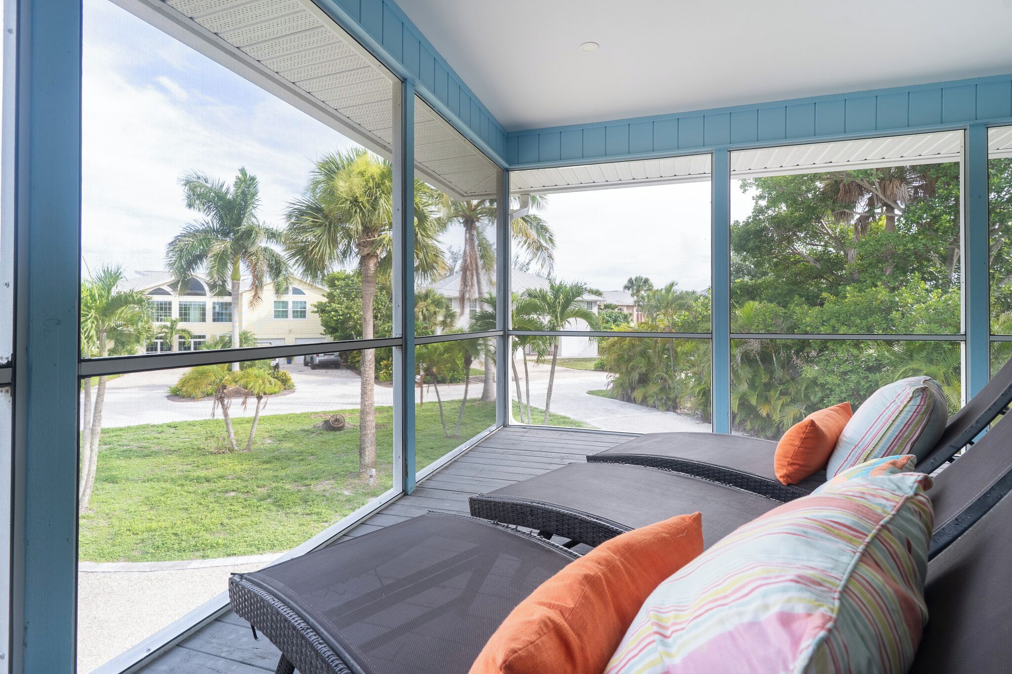 A room with a large window, a sofa with cushions, and a view of a green landscape with palm trees.