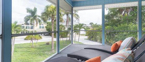 A room with a large window, a sofa with cushions, and a view of a green landscape with palm trees.